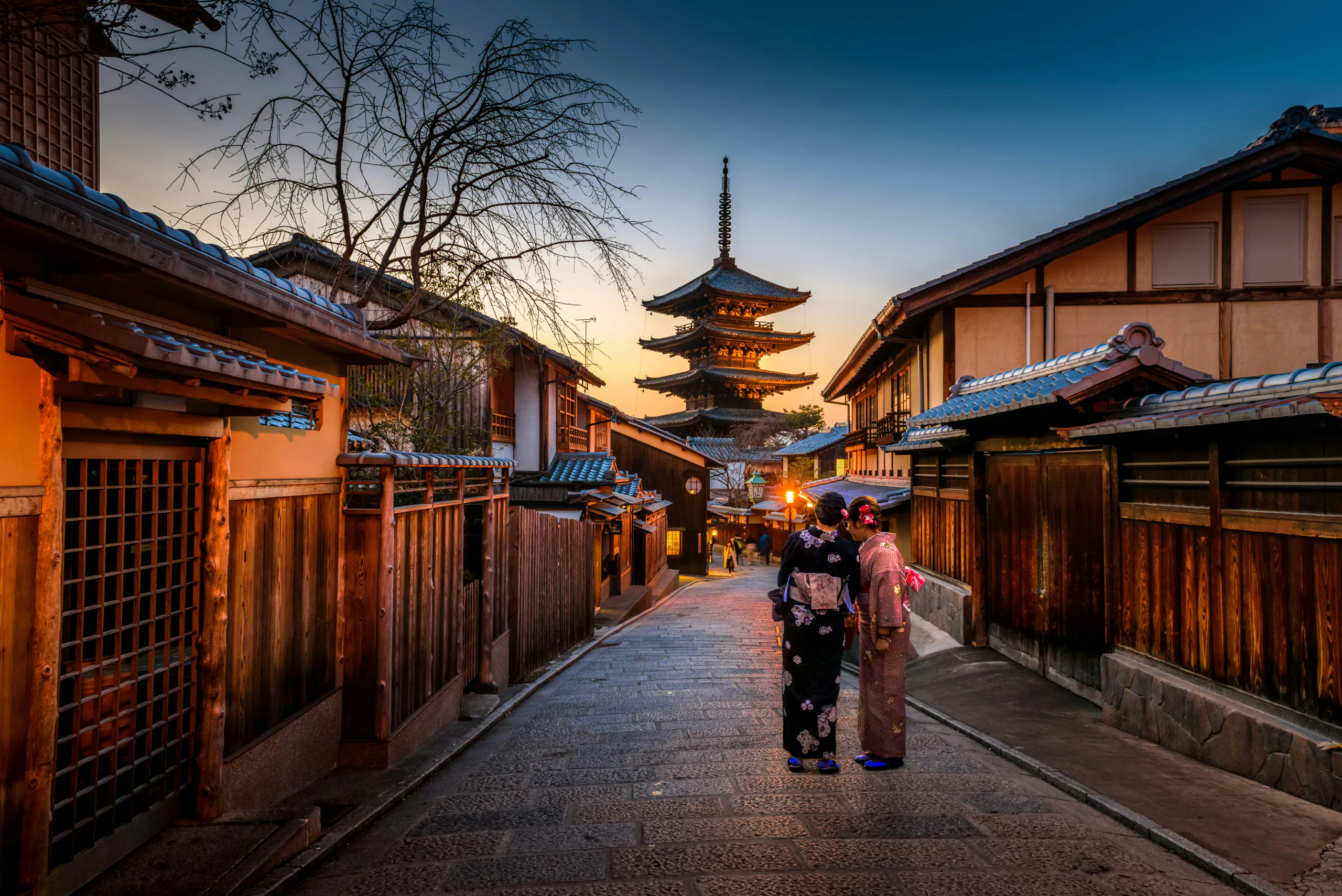 Two women in kimono on a stone street in Kyoto, with Yasaka Pagoda at sunset